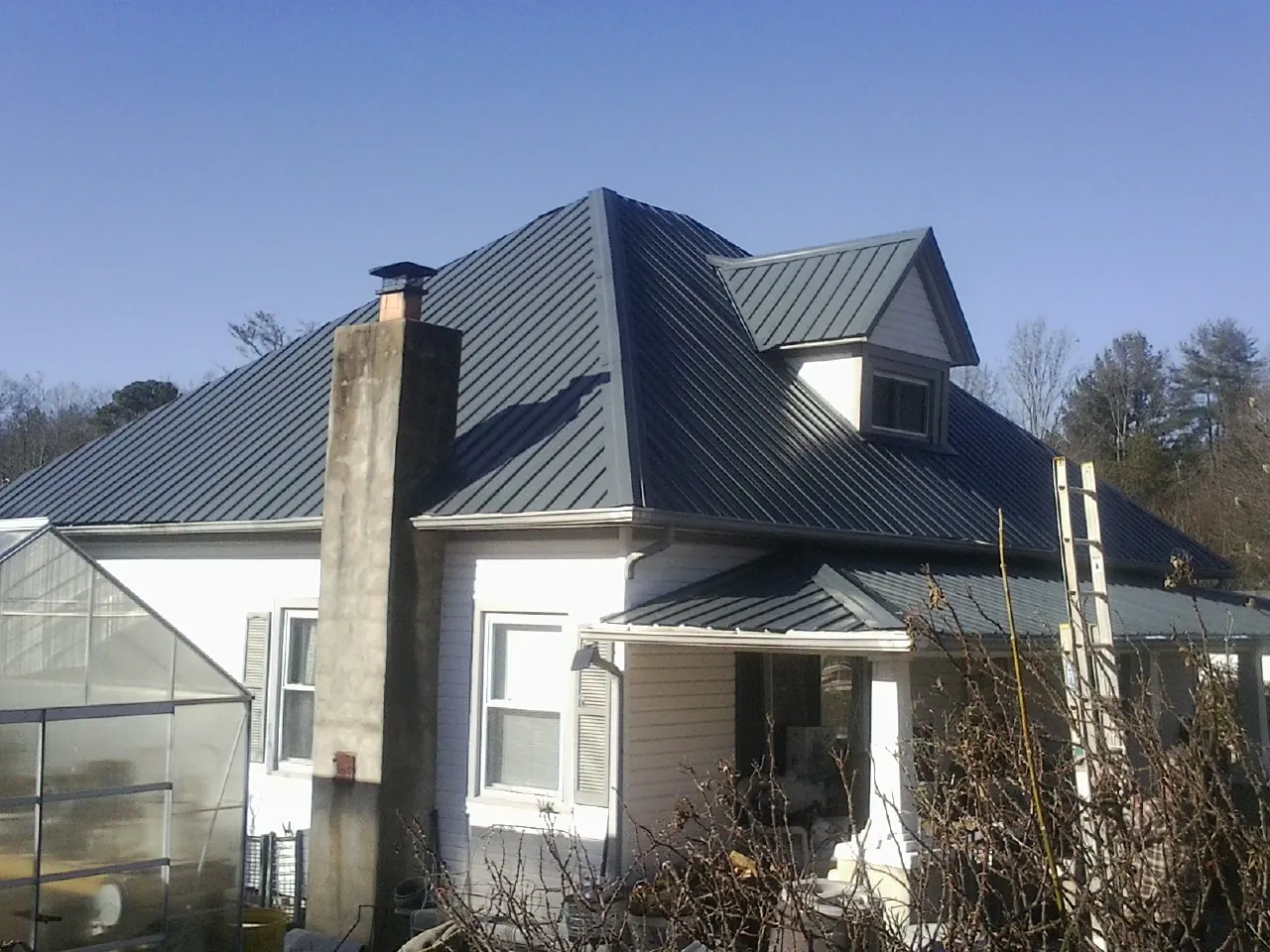 Dark blue standing seam metal roof on a white farmhouse with dormer — Slate & Tile Roof Repair by Roofing Brothers in Fonda