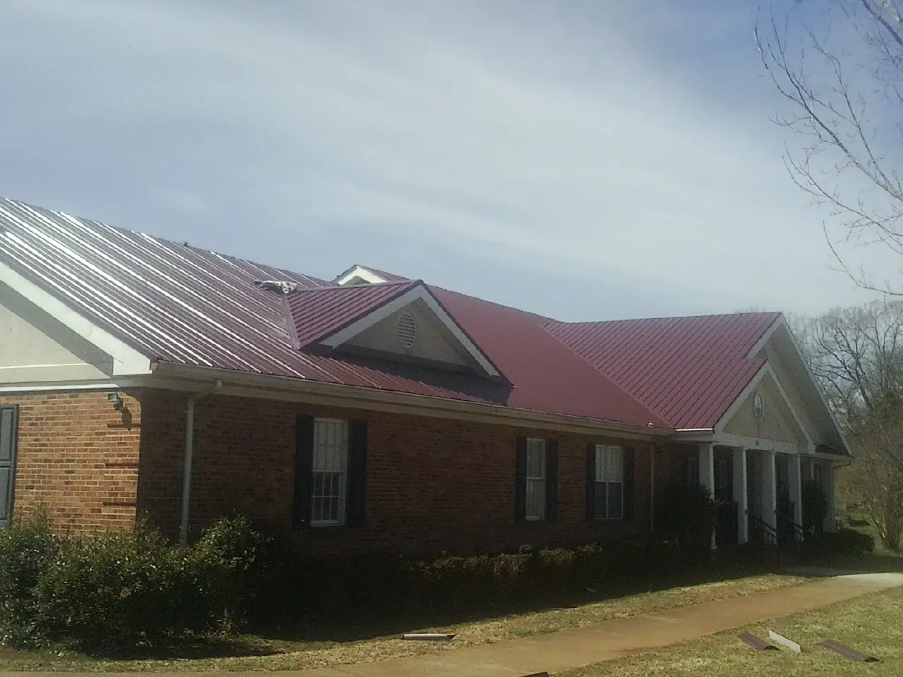 Red metal roof with gabled entries on a long brick building, from a Hail Damage Roof Repair job in Fonda