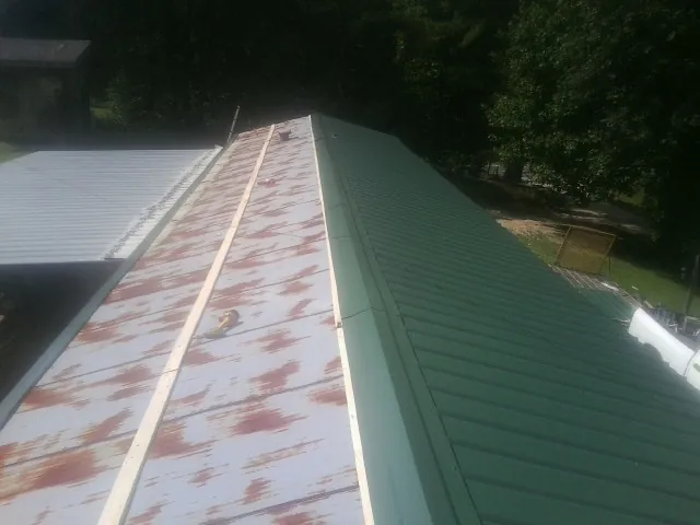 Old rusted panels beside newly installed green metal roofing — Wind Damage Roof Repair by Roofing Brothers in Fonda