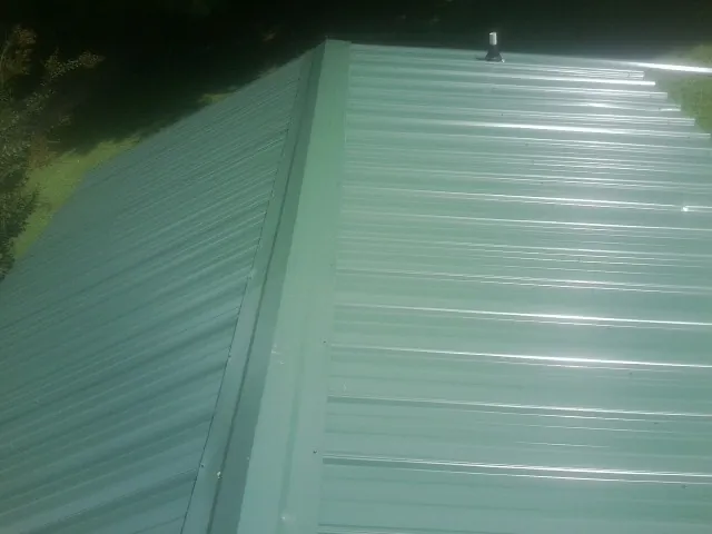 New green metal panels meeting at the ridge of a roof — Flat Roof Repair work by our crew in Fonda
