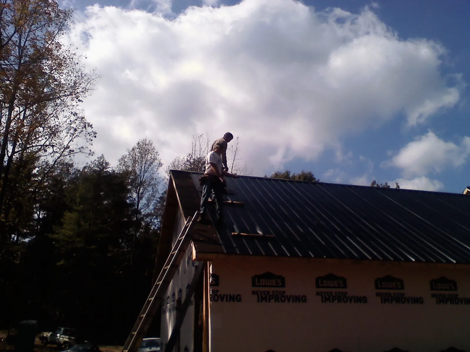 Roofer fastening dark metal panels high against a cloudy sky, from a Roof Inspection job in Fonda