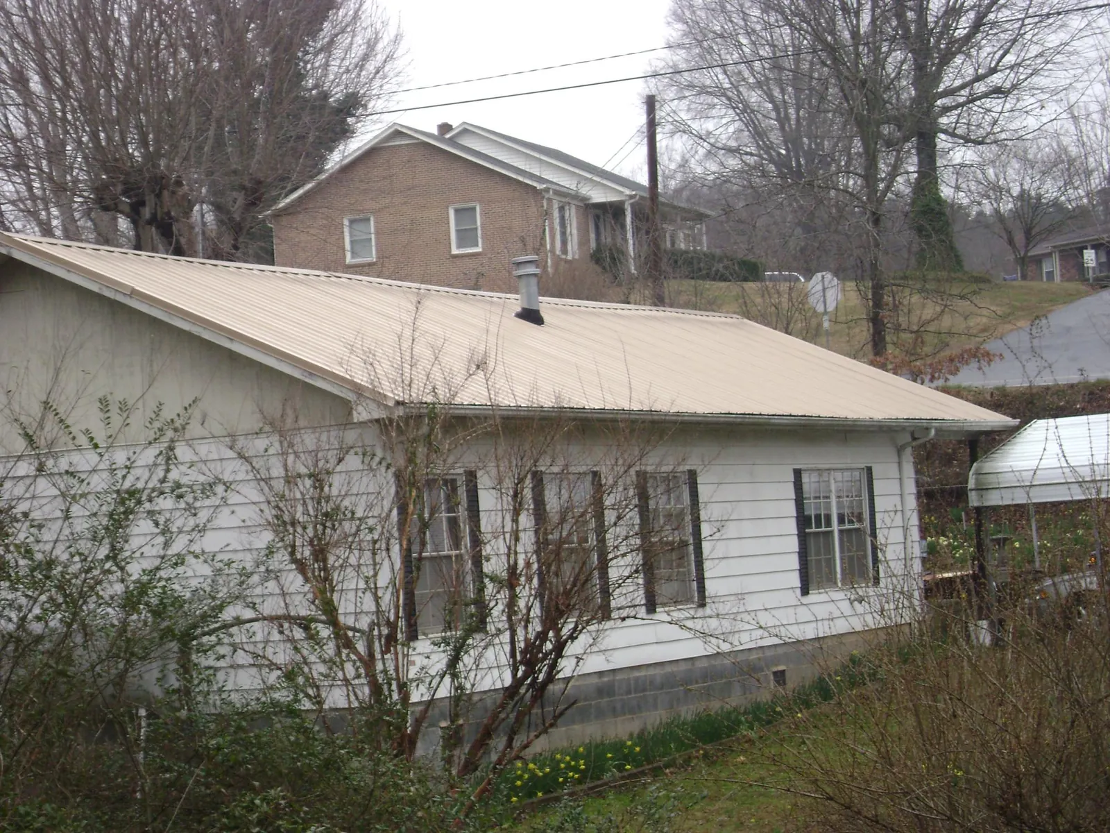Tan metal roof on a white sided house set into a hillside — Commercial Roofing by Roofing Brothers in Fonda