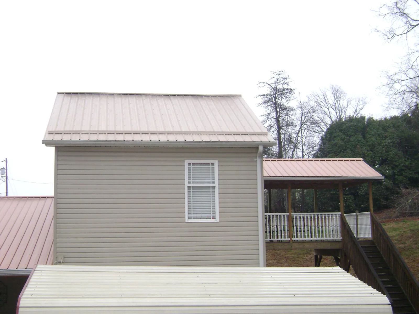 Tan metal roofs on a two story addition and attached porch, from a Roof Replacement job in Fonda